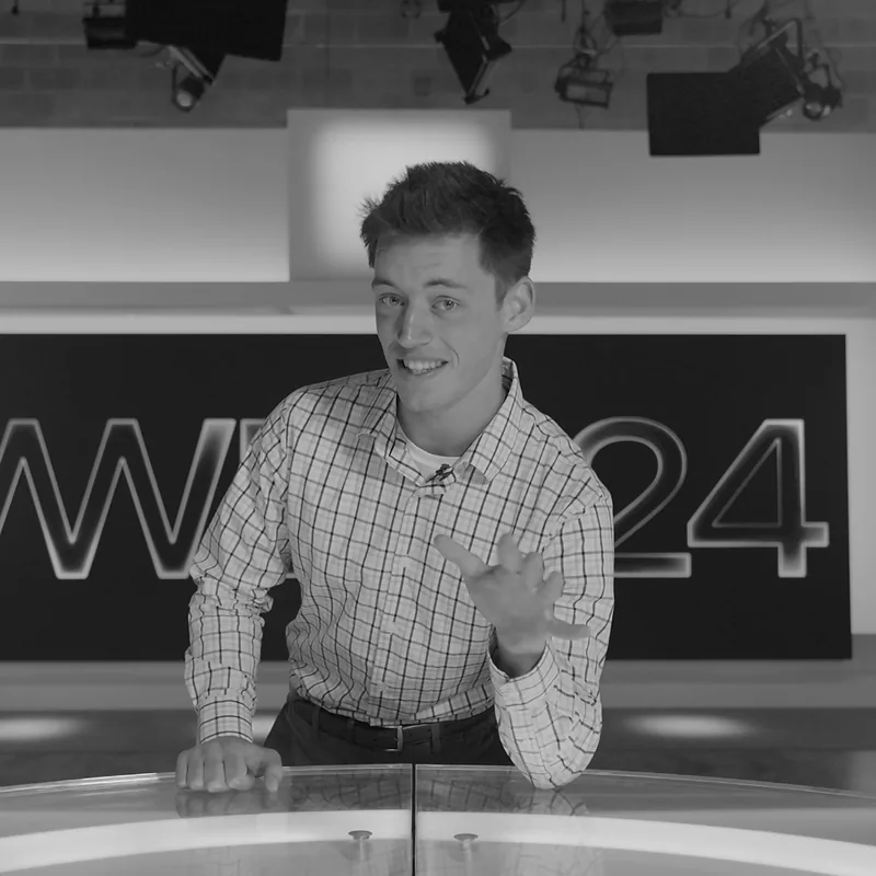 Frank Palmieri, founder of Frank Palmieri Media, at a television news anchor desk — black-and-white portrait.